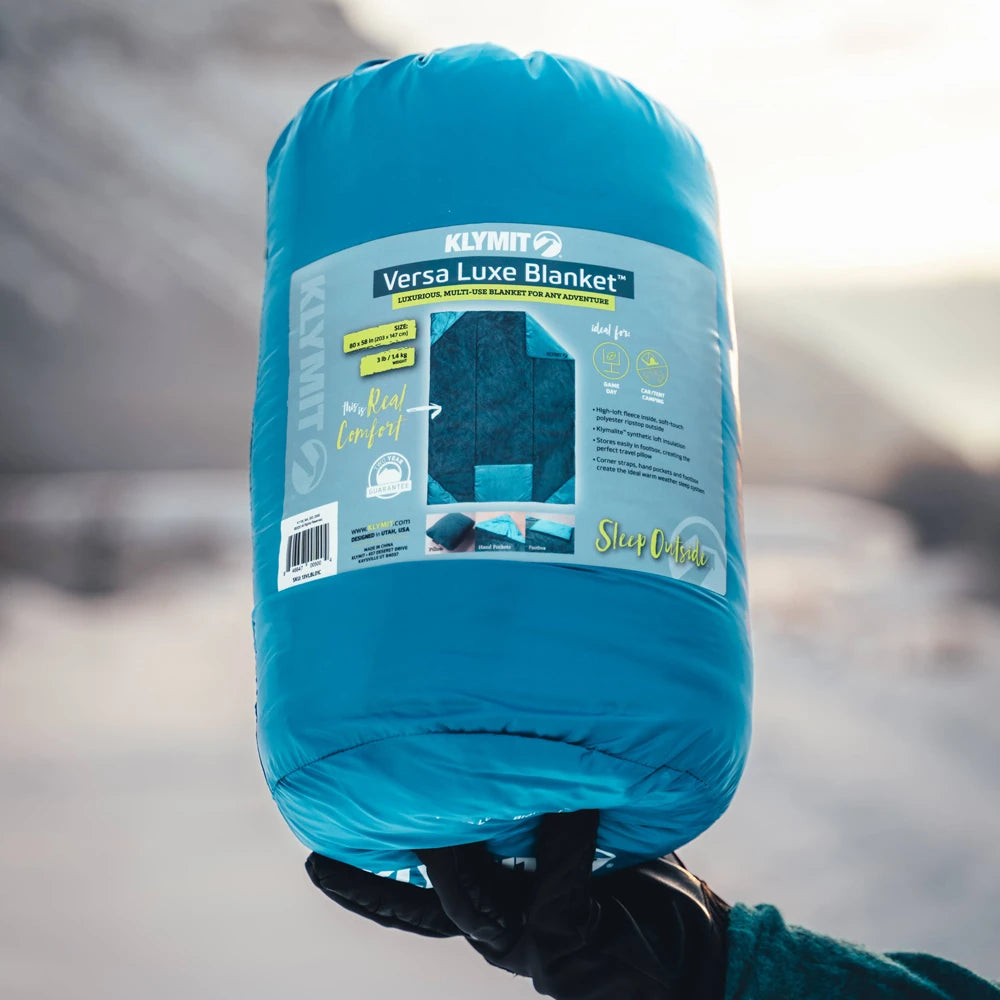 Klymit Versa Luxe Blanket in packaging held by a person with a blurred natural background