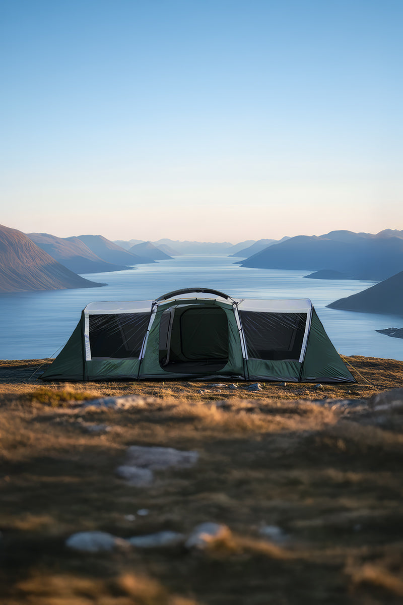 Camping tent set up on a grassy area with a scenic view of mountains and water.