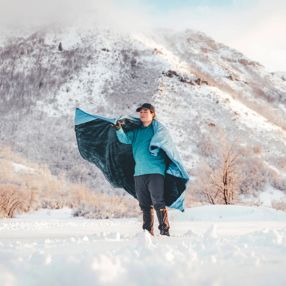 Person holding a blue blanket in a snowy landscape with mountains in the background